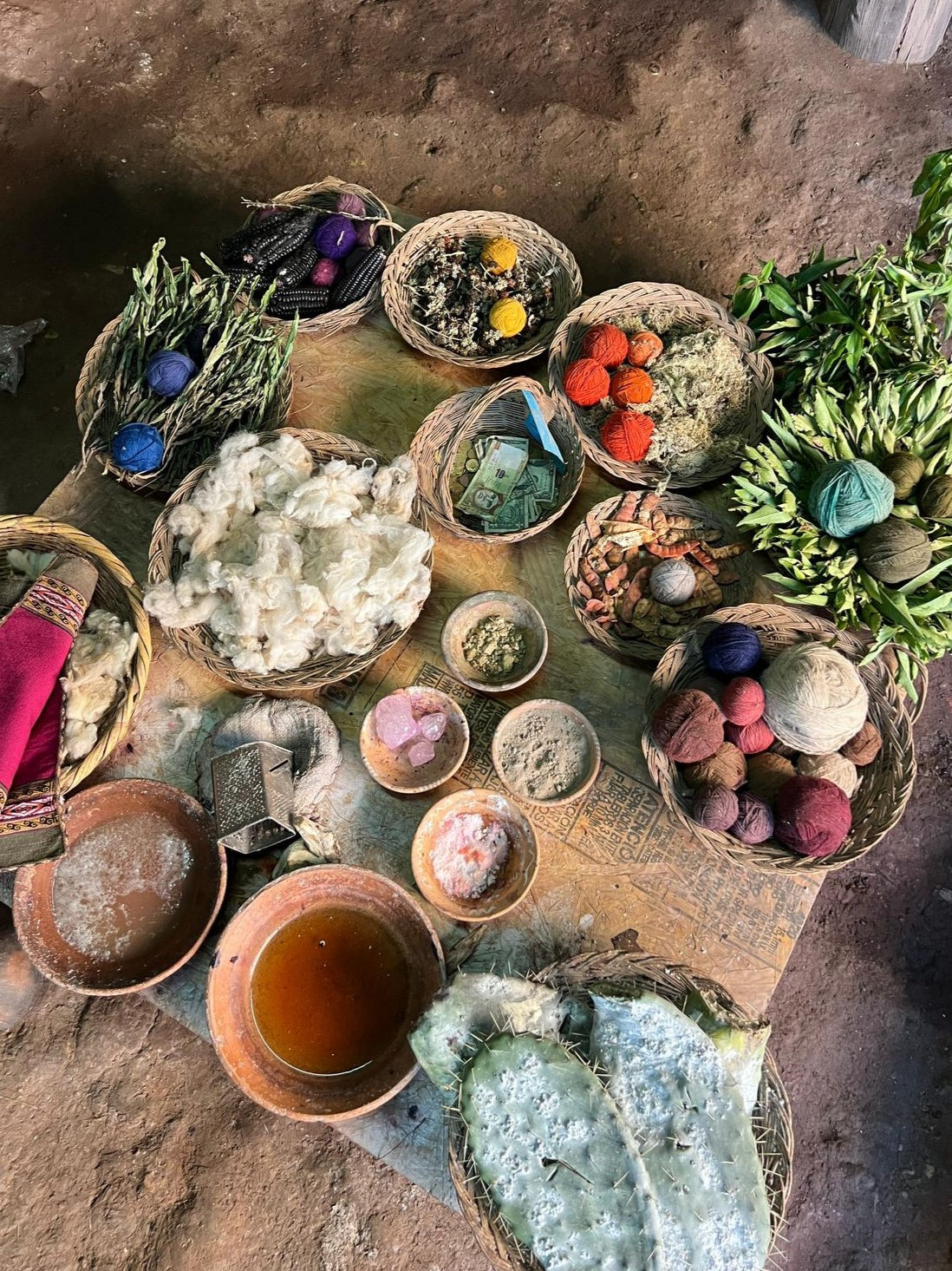 A vibrant display of natural dyes and wool in Chinchero, Cusco. Colorful skeins of wool are arranged on a table, alongside bowls and pots filled with natural dye substances. The scene showcases traditional Andean dyeing techniques with vivid reds, yellows, blues, and greens, highlighting the region's rich cultural heritage and craftsmanship. Traditional textiles and tools used in the dyeing process are visible in the background.