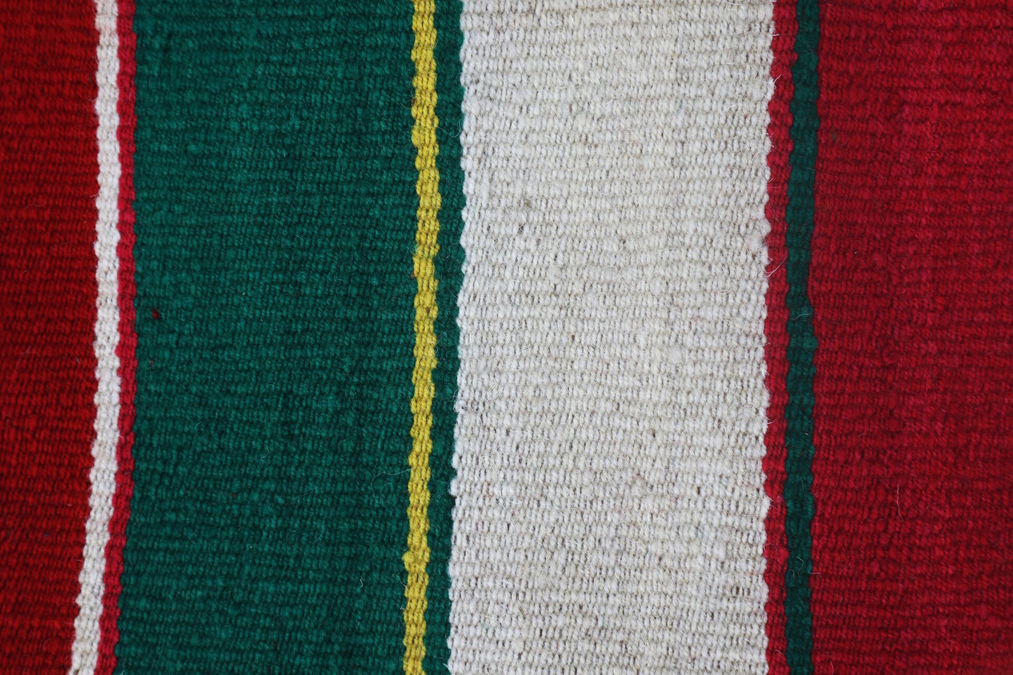 A folded Peruvian handmade blanket featuring vibrant red, green, and white colors