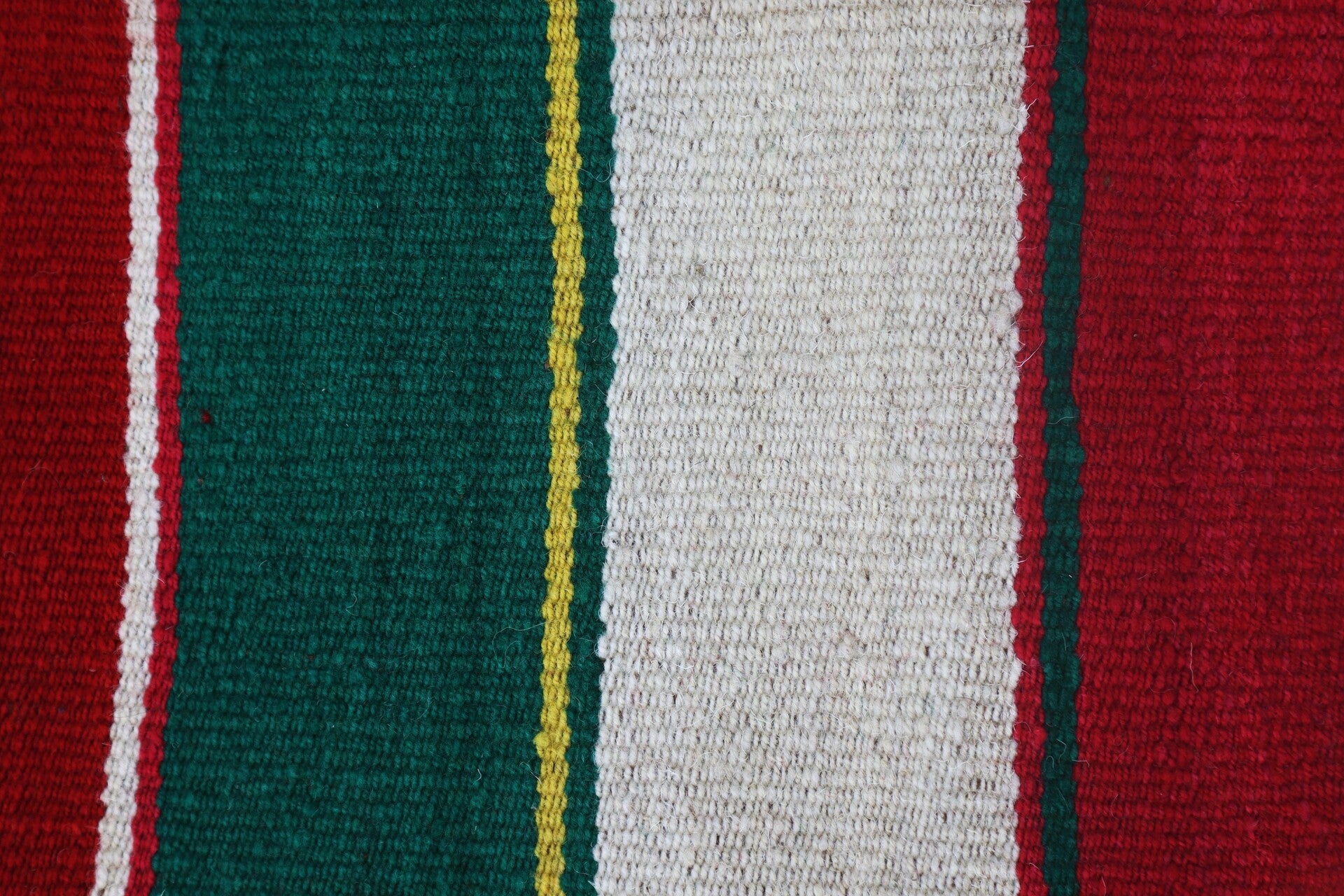 A folded Peruvian handmade blanket featuring vibrant red, green, and white colors