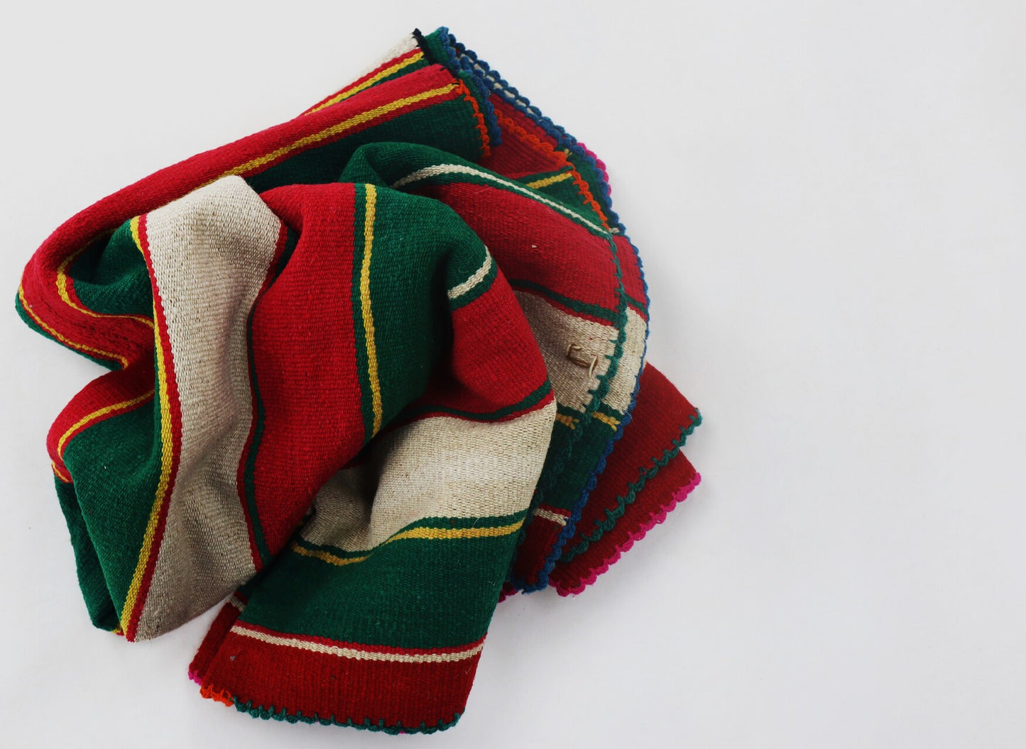 A folded Peruvian handmade blanket featuring vibrant red, green, and white colors