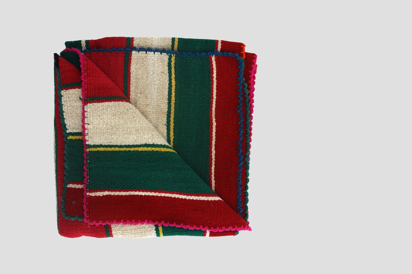 A folded Peruvian handmade blanket featuring vibrant red, green, and white colors